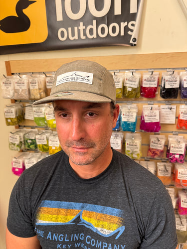 Man wearing a cap and t-shirt with an Angling Company logo in front of a store shelf.